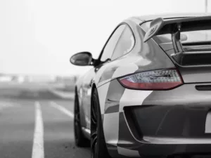 Fotografía Porsche 997 GT3 3.8 en blanco y negro con técnica de color selectivo, único punto de color en los faros traseros rojos bajo cielo nublado, fotografía artística moody edición limitada