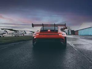 Porsche 911 GT3 RS 992 rojo visto desde atrás en pista de carreras al amanecer con cielo rojizo y anaranjado, alerón trasero prominente y frenos cerámicos visibles