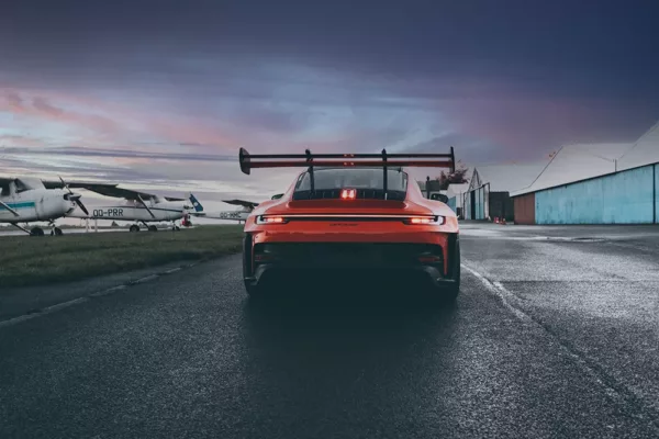 Fotografía Porsche GT3 RS y amanecer Porsche 911 GT3 RS 992 rojo visto desde atrás en pista de carreras al amanecer con cielo rojizo y anaranjado, alerón trasero prominente y frenos cerámicos visibles