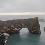 Foto decoración mural del arco natural de Dyrhólaey en Islandia mostrando el acantilado negro y el océano bajo un cielo dramático, perfecta para decoración interior nórdica