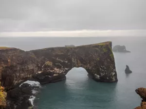 Foto decoración mural del arco natural de Dyrhólaey en Islandia mostrando el acantilado negro y el océano bajo un cielo dramático, perfecta para decoración interior nórdica