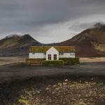 Restaurante solitario blanco cubierto de musgo en tierras altas volcánicas negras Möðrudalsleið Islandia, montañas dramáticas cielo nublado, paisaje nórdico desolado contemplativo