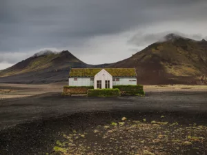 Restaurante solitario blanco cubierto de musgo en tierras altas volcánicas negras Möðrudalsleið Islandia, montañas dramáticas cielo nublado, paisaje nórdico desolado contemplativo