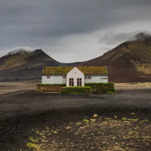 Restaurante solitario blanco cubierto de musgo en tierras altas volcánicas negras Möðrudalsleið Islandia, montañas dramáticas cielo nublado, paisaje nórdico desolado contemplativo