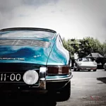Foto Porsche 911 Type 901 azul turquesa en primer plano mostrando la parte trasera del vehículo con inscripción "Porsche 911", faro redondo y otro Porsche classic blanco al fondo, fotografía artística Cars and Roses