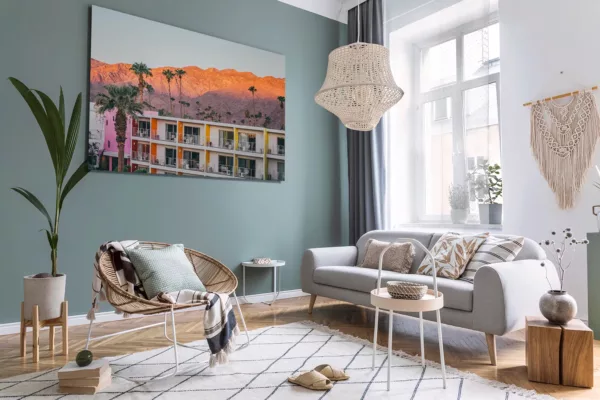 Fotografía enmarcada del hotel The Saguaro Palm Springs al atardecer exhibida en salón escandinavo moderno con pared verde salvia, sofá gris claro, silla de ratán yación bohemia decor