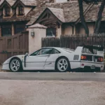 Tiraje de arte Ferrari F40 blanco exhibido en gran lona sobre pared de ladrillos azul claro en salón moderno minimalista con sillones blancos, mesa geométrica y luz natural