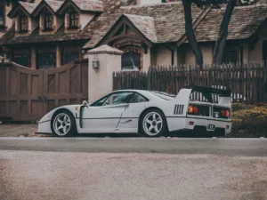 Tiraje de arte Ferrari F40 blanco exhibido en gran lona sobre pared de ladrillos azul claro en salón moderno minimalista con sillones blancos, mesa geométrica y luz natural