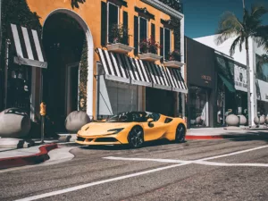 Fotografía de Ferrari F488 Spider amarilla estacionada en Rodeo Drive, con edificios de fondo y palmeras, vista lateral del vehículo en un entorno urbano luminoso.