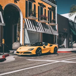 Fotografía de Ferrari F488 Spider amarilla estacionada en Rodeo Drive, con edificios de fondo y palmeras, vista lateral del vehículo en un entorno urbano luminoso.