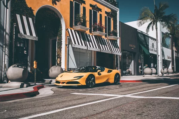 Fotografía de Ferrari F488 Spider amarilla estacionada en Rodeo Drive, con edificios de fondo y palmeras, vista lateral del vehículo en un entorno urbano luminoso.