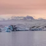 Icebergs azul celeste flotando en laguna glaciar Jökulsárlón Islandia bajo cielo crepuscular rosa delicado con vasto glaciar fondo, paisaje nórdico sereno contemplativo