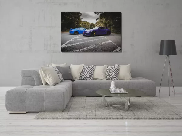 Salón moderno con cuadro grande de Porsche 991 GT3 y GT3 RS colgado en la pared, sofá gris con cojines claros y de cebra, café circular y alfombra suave, decoración contemporánea. mesa de