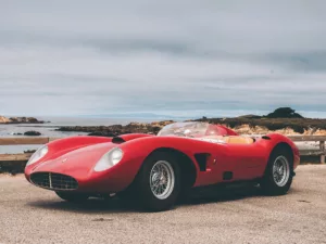 Imagen 2: Fotografía de Ferrari Testarossa roja en una carretera costera, con matrícula visible, cielo nublado y paisaje marítimo al fondo, vista lateral del vehículo.