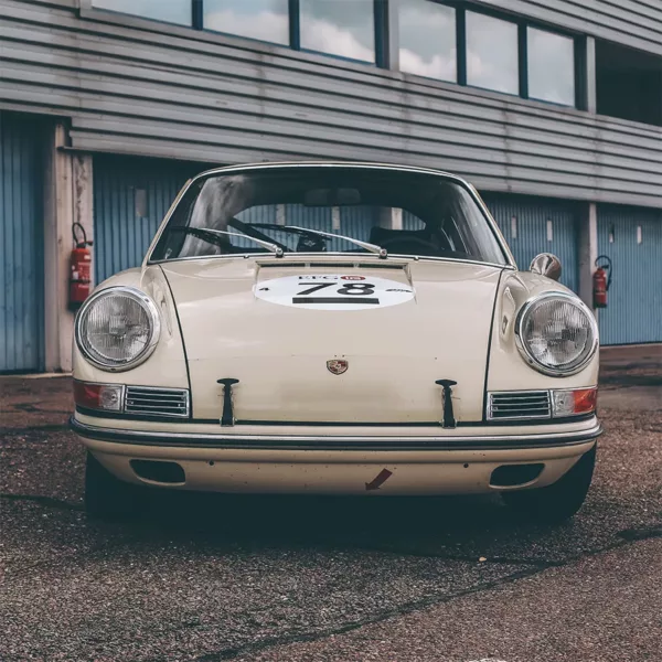 Porsche 911 Clásico blanco de competición en pits del circuito Dijon-Prenois, fotografía artística en blanco y negro con acabado moody vintage, jaula antivuelco y detalles racing visibles