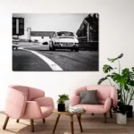 Salón moderno con cuadro grande de Porsche 911 Carrera blanco y negro en circuito colgado en pared beige, dos sillones rosas, mesa redonda de madera y plantas verdes, decoración interior contemporánea