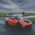 Fotografía de arte del Porsche 911 GT3 RS naranja en pista de aviación con avión Beechcraft Bonanza