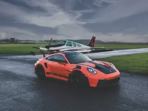 Fotografía de arte del Porsche 911 GT3 RS naranja en pista de aviación con avión Beechcraft Bonanza