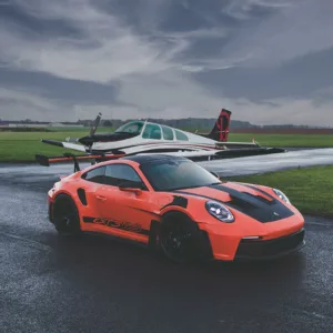 Fotografía de arte del Porsche 911 GT3 RS naranja en pista de aviación con avión Beechcraft Bonanza