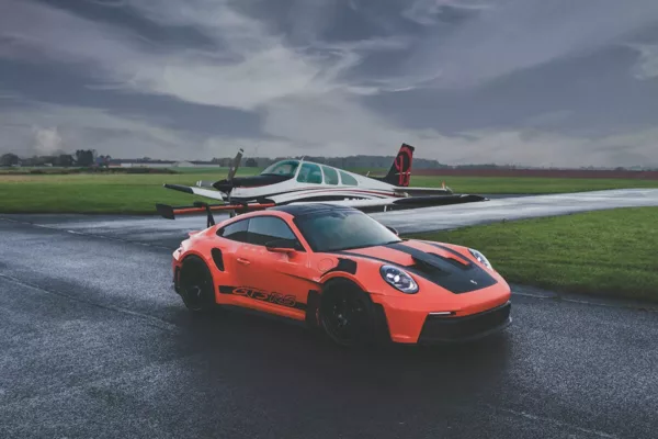 Fotografía de arte del Porsche 911 GT3 RS naranja en pista de aviación con avión Beechcraft Bonanza