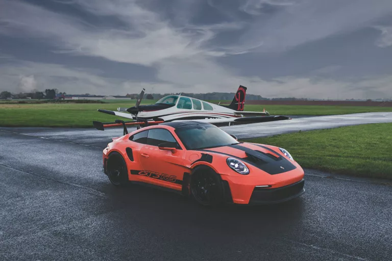 Fotografía de arte del Porsche 911 GT3 RS naranja en pista de aviación con avión Beechcraft Bonanza