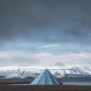 Fotografía del Svalbard con tienda solitaria frente a los fiordos árticos nevados bajo un cielo dramático