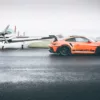 Porsche 911 GT3 RS naranja sobre pista mojada de aeródromo, junto a avioneta ligera - cuadro fotográfico