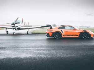 Piste Mouillée Wall ARt Porsche GT3 Rs Porsche 911 GT3 RS naranja sobre pista mojada de aeródromo, junto a avioneta ligera - cuadro fotográfico