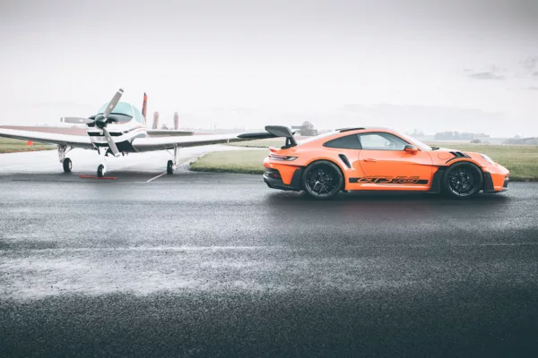 Porsche 911 GT3 RS naranja sobre pista mojada de aeródromo, junto a avioneta ligera - cuadro fotográfico